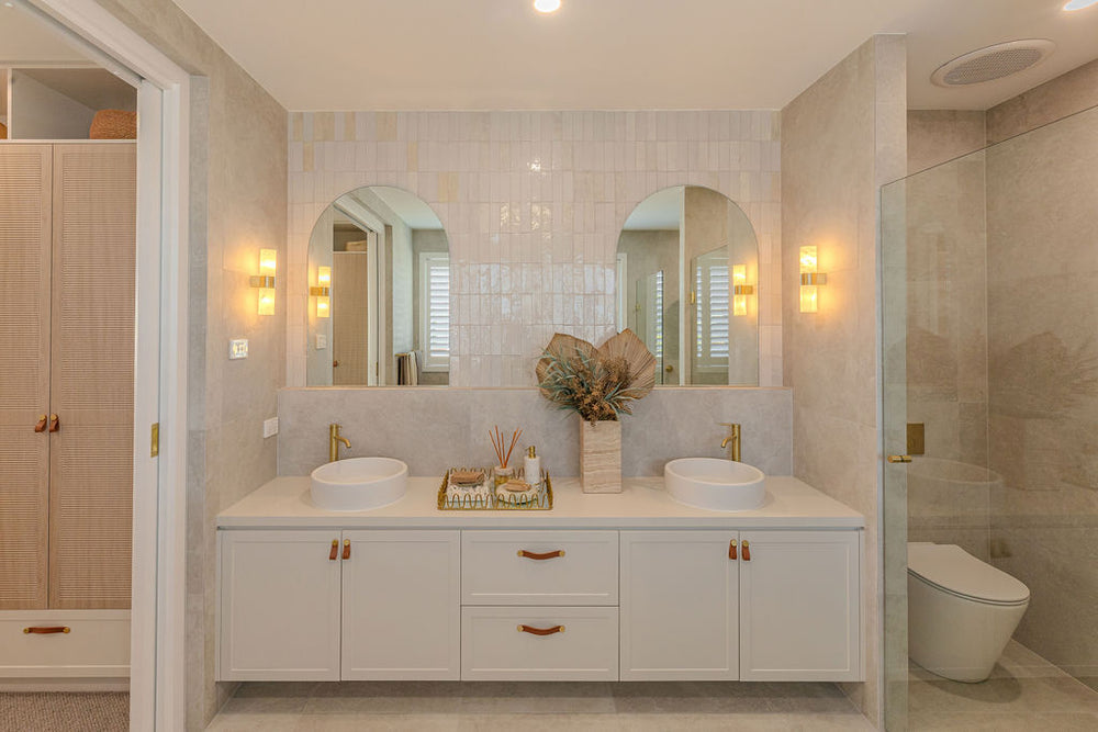 Modern bathroom with white vanity, shaped mirrors, and a shower.