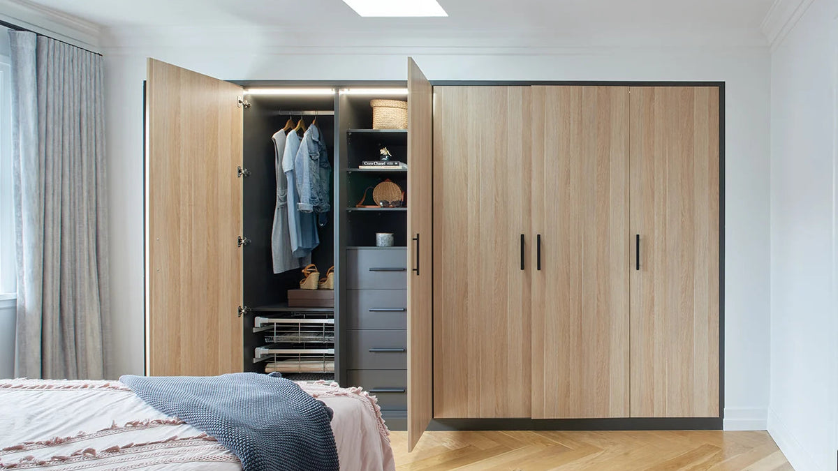Wooden hinged wardrobe with open doors revealing clothes and shelves in a bedroom.